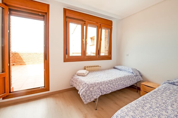 A bedroom with a single bed, a small bedside table, a radiator, and a window with wooden frames.