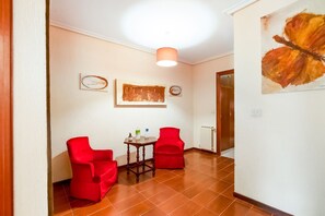 A hallway with two red chairs, a small table with bottles, and a painting on the wall. - Belvilla by OYO Casa rural (laguardia)