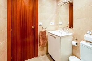 A bathroom with a wooden door, a white sink, a mirror, and a toilet.