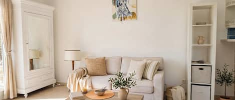 Una sala de estar con sofá, mesa de centro, lámpara, un cuadro y un aparador.
