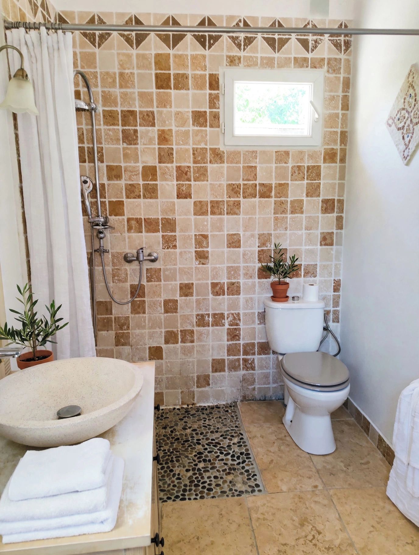 A bathroom with a shower, toilet, sink, and a window.