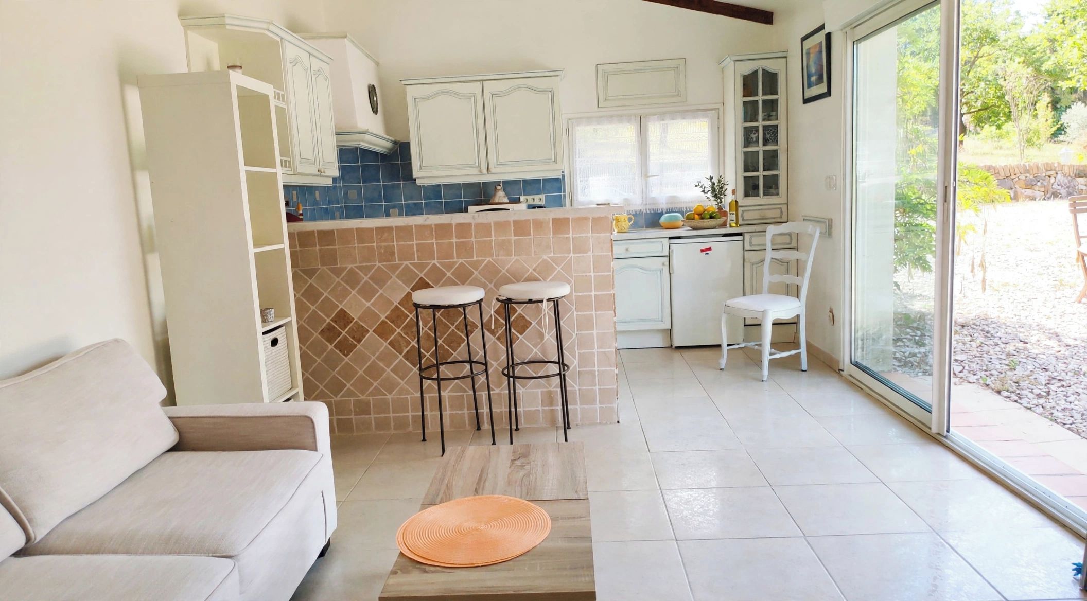 A modern kitchen with white cabinets, a blue backsplash, and a dining area with a white chair and stools.