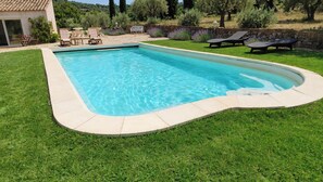 A rectangular swimming pool with a curved edge, surrounded by a well-maintained lawn and a stone wall.