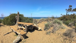 A wooden structure with a bench, surrounded by sand and sparse vegetation.