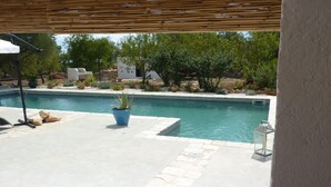 A pool area with a pergola, potted plants, and a stone pathway.