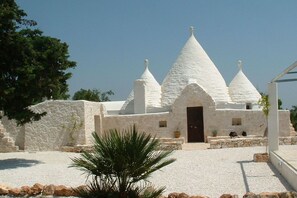 Un bâtiment blanc doté d’un toit conique et d’une porte centrale, entouré de gravier et d’un palmier.