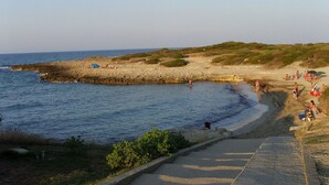 A coastal beach with a rocky shoreline, a sandy area with people and tents, and a clear sky.