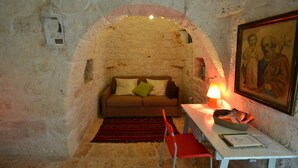 A cozy room with a stone wall, a sofa with cushions, a red chair, a table with a lamp, and a framed painting.