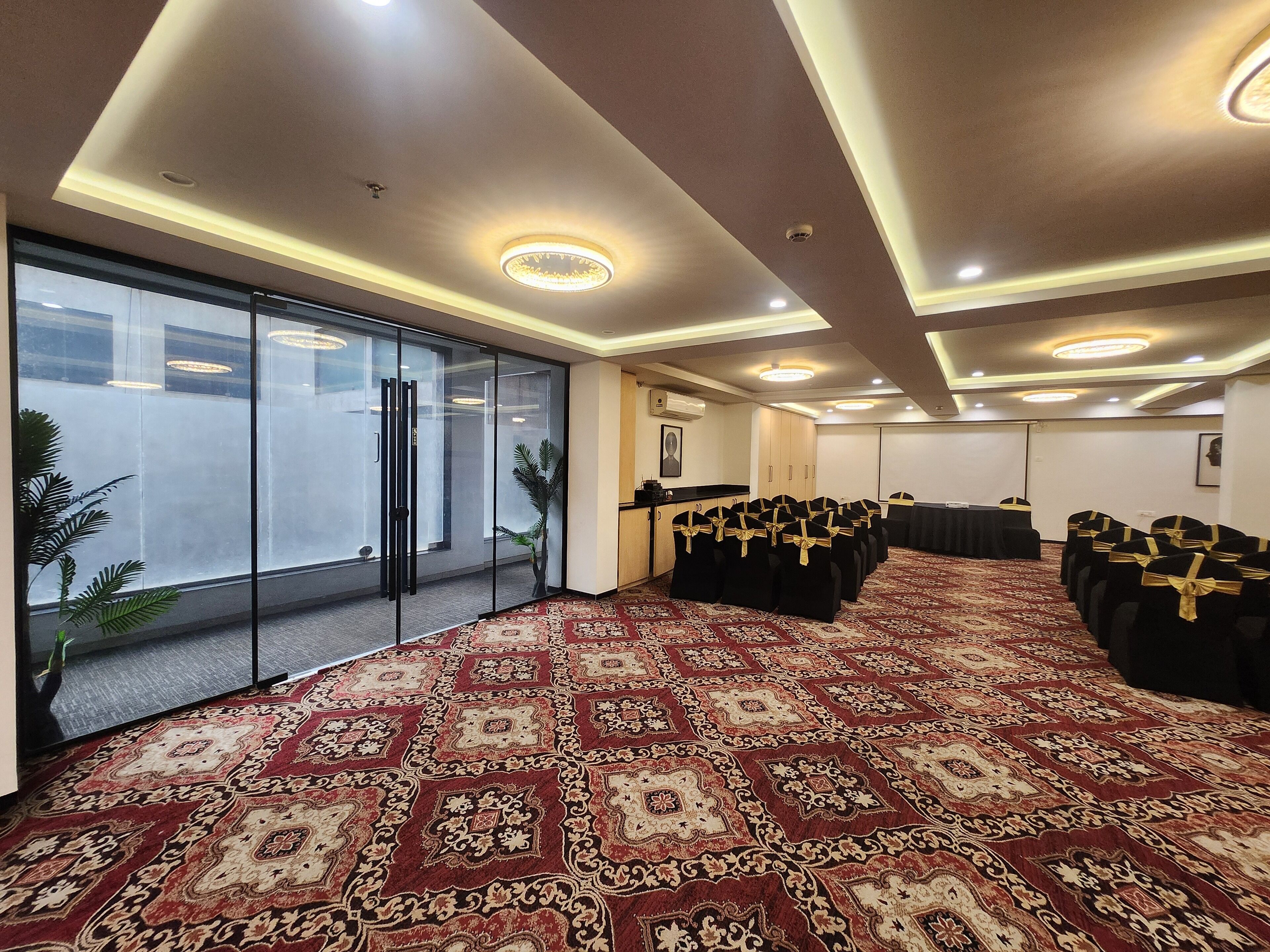 Un salón de conferencias con alfombra estampada, sillas negras con cintas doradas y un ventanal con vistas.