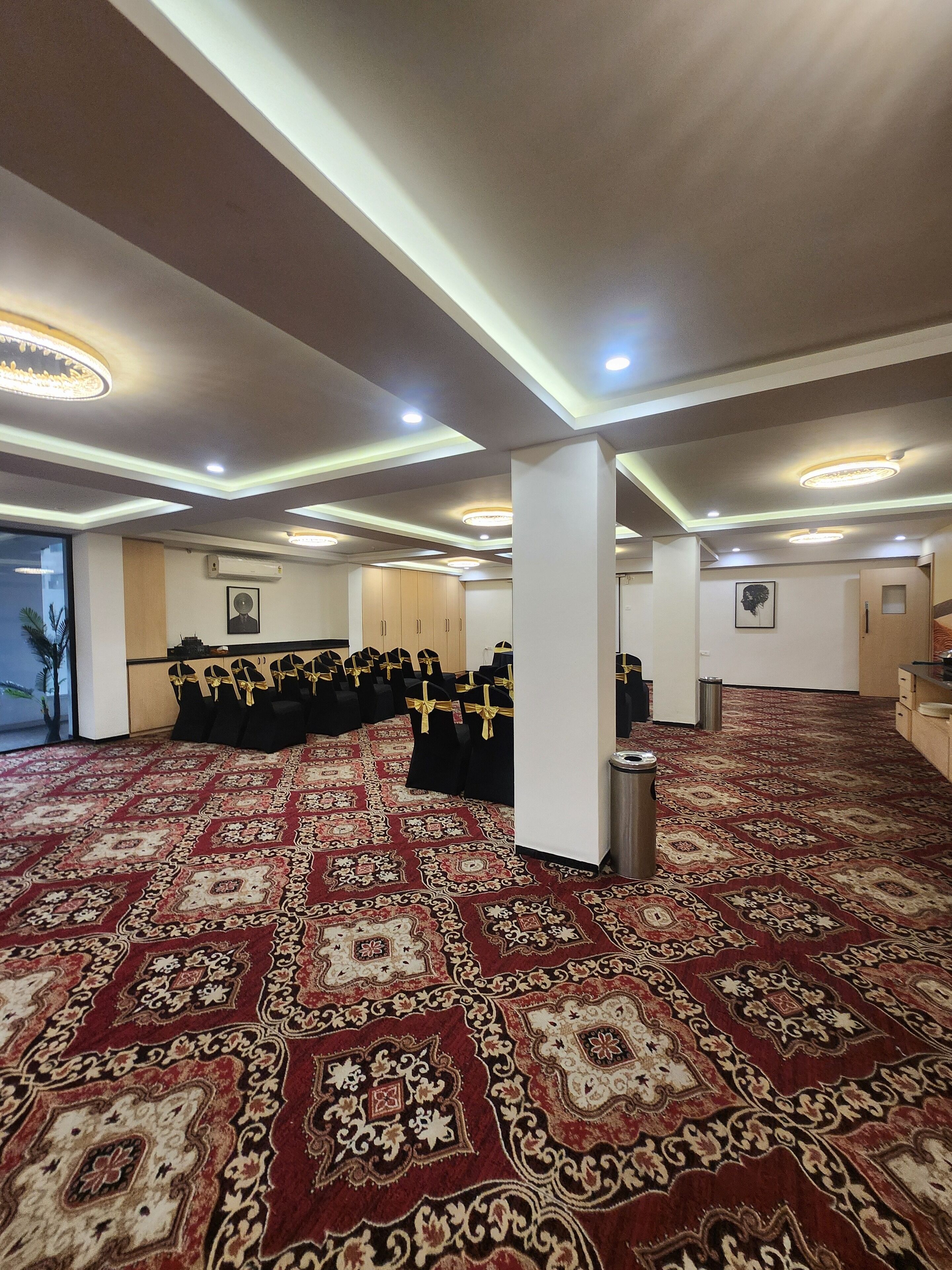 A spacious hall with a patterned carpet, rows of black chairs with gold sashes, and recessed lighting on the ceiling.