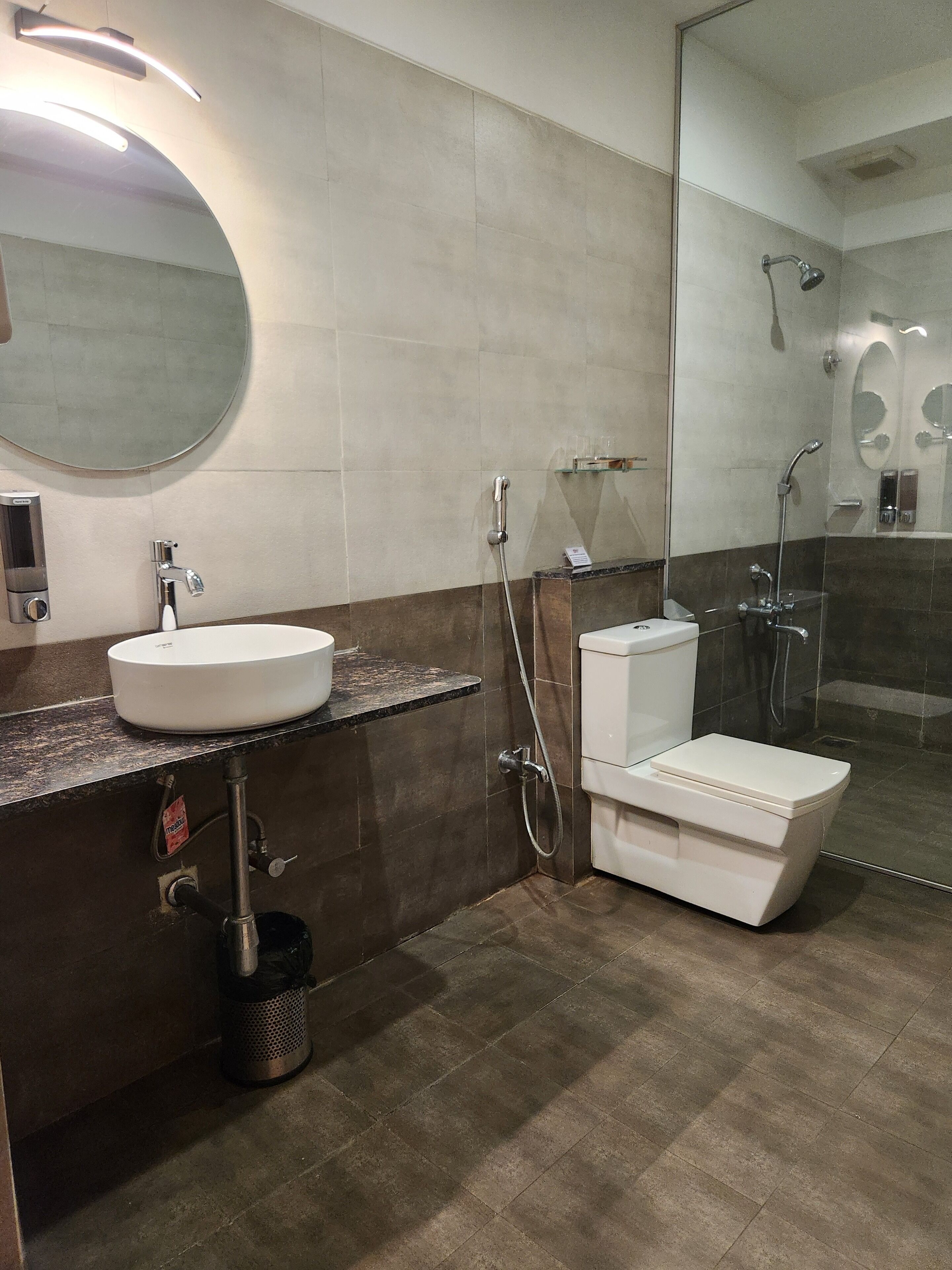 A modern bathroom with a round mirror, a white sink, a toilet, and a shower area.