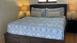A bedroom with a bed, two bedside lamps, a ceiling fan, a window with shutters, and a built-in nightstand. - Hidden Treasure - located ON the boardwalk! (Christiansted)