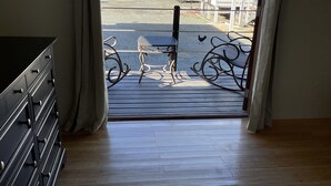 A room with a wooden floor, a black dresser, and a view through a door to a balcony with a railing and a chair. - Hidden Treasure - located ON the boardwalk! (Christiansted)