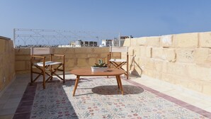 Eine kleine Terrasse im Freien mit einem Holztisch und -stühlen, einem Blumentopf und einem dekorativen Fliesenboden.