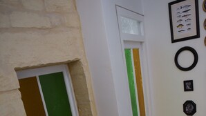 Ein Korridor mit einer Steinsäule, einer Tür mit grün-goldenen Verzierungen, einem gemusterten Teppich und einer gerahmten Illustration von Fischen an der Wand.