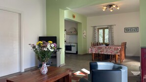 Una sala de estar con una mesa de centro de madera, un jarrón de flores y un comedor con una mesa lista para cuatro.