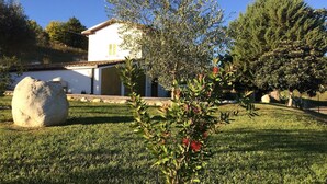 Una casa con techo de tejas, un pequeño jardín con un árbol y un arbusto, y una roca grande al frente.