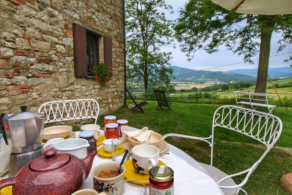 A rustic outdoor dining setup with stone walls, a table with various dishes and utensils, and a scenic view of hills in the background.