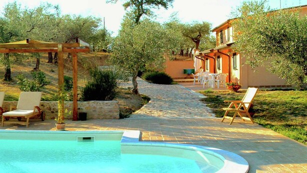 Una piscina con sillones de descanso, una pérgola y un sendero que lleva a un edificio con terraza.