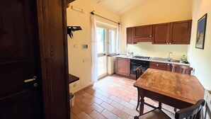 Cocina pequeña con armarios de madera, suelo de baldosas, mesa de comedor y una ventana con cortinas.