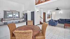 En rummelig opholdsstue med spisebord og stole, et køkken med moderne hårde hvidevarer, en trappe og en blå sofa.