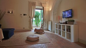 Un salon comprenant un téléviseur, un fauteuil en osier, un canapé bleu et une étagère blanche.