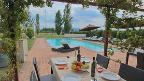 Une table à manger pour deux, avec vue sur la piscine, des chaises d’extérieur et une pergola couverte de plantes grimpantes.