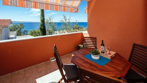 Ein Balkon mit Holztisch, Stühlen und einer Weinflasche.