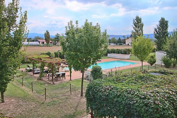 Un espace piscine agrémenté d’une pergola et de sièges, entouré de verdure et offrant une vue sur les collines lointaines.