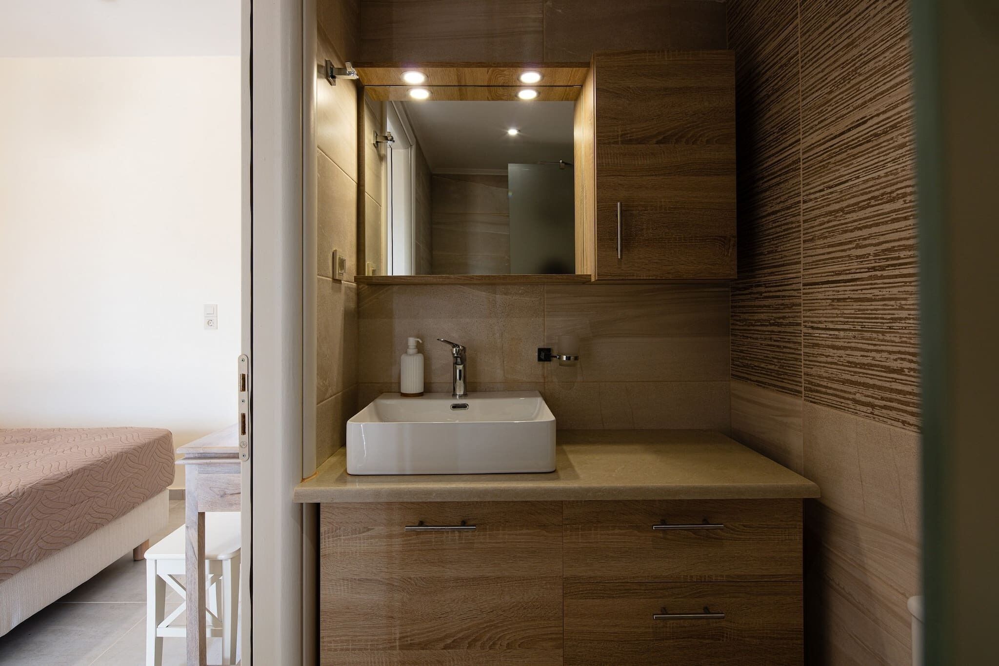 A modern bathroom with a wooden vanity, a white sink, and a mirror above it.