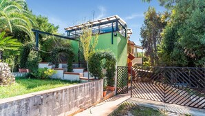 Una casa moderna con fachada verde, un invernadero de vidrio y un portón metálico.