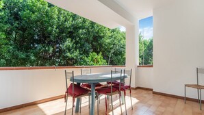 Un balcón con mesa y sillas, vistas a árboles verdes exuberantes y suelo de baldosas.