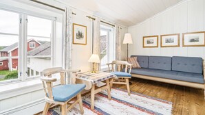 Una habitación acogedora con una mesa de madera, sillas, un sofá azul y vistas a casas a través de amplias ventanas.