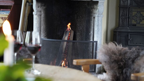 Una habitación acogedora con chimenea, una silla de madera y una copa de vino tinto.