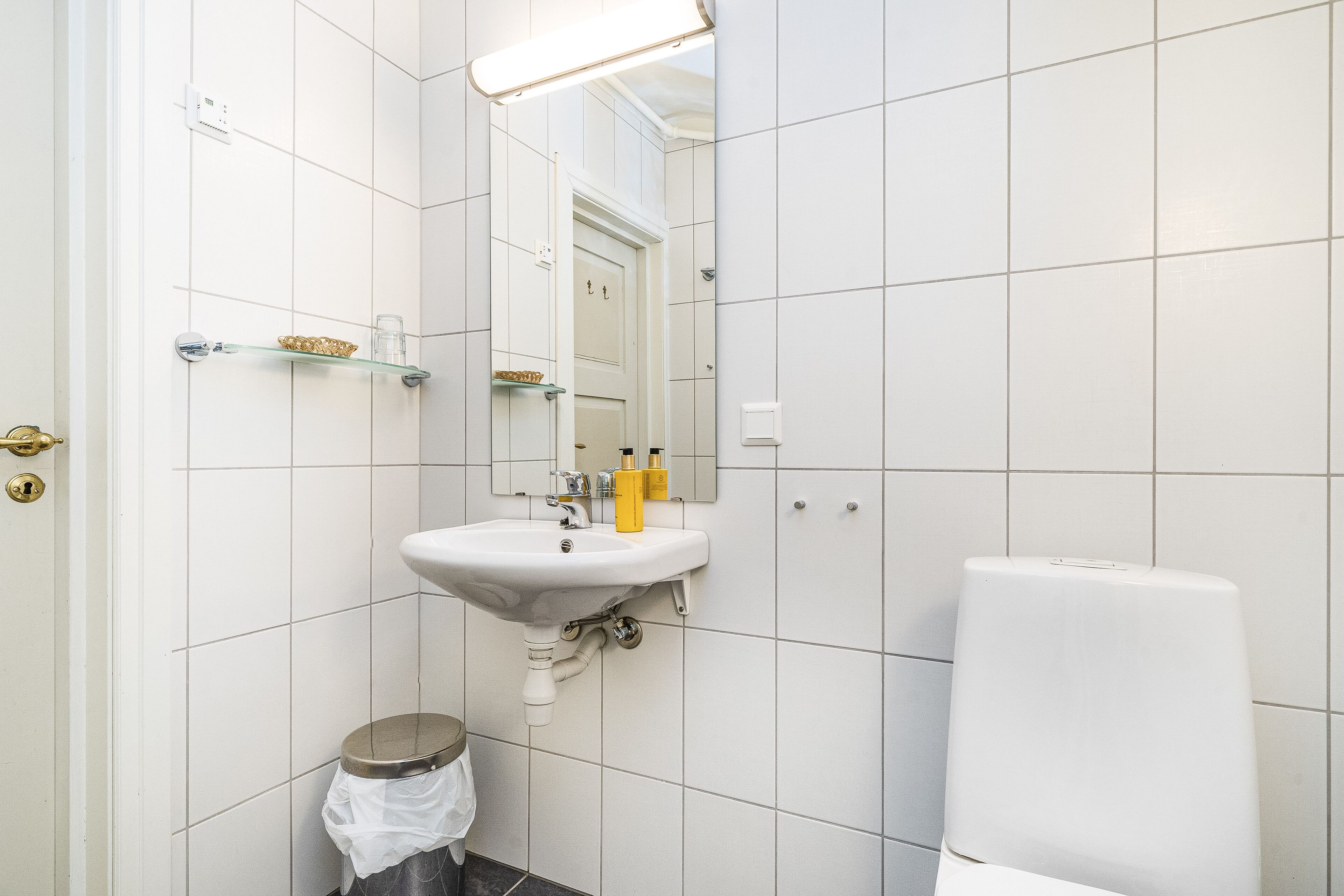 A bathroom with white tiled walls, a white sink with a mirror above it, and a toilet.