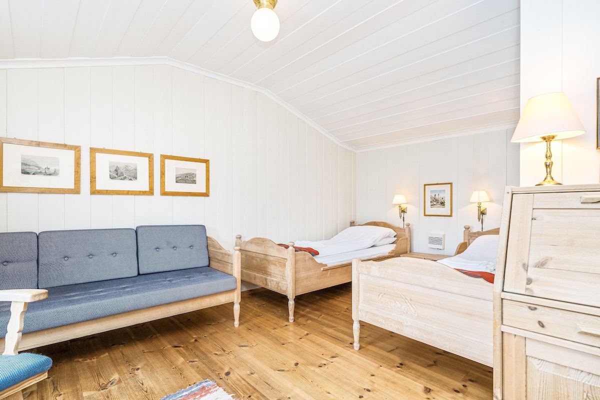 Habitació amb un sòl de fusta, un sofà blau, un llit de fusta i un armari de fusta.