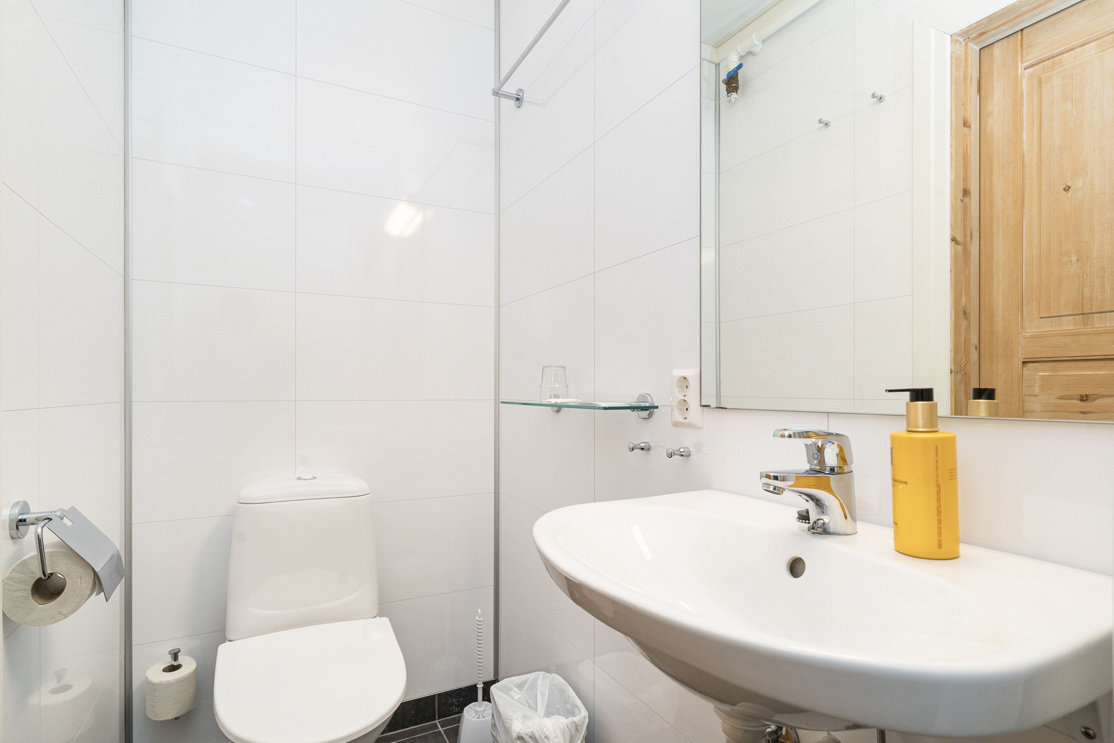 Een badkamer met een witte wastafel, een douchecabine van glas, een toilet en een houten kastje boven de spiegel.