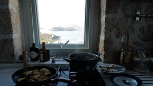 Une cuisine donnant sur la mer, une casserole sur la cuisinière, et diverses bouteilles et assiettes sur le plan de travail.