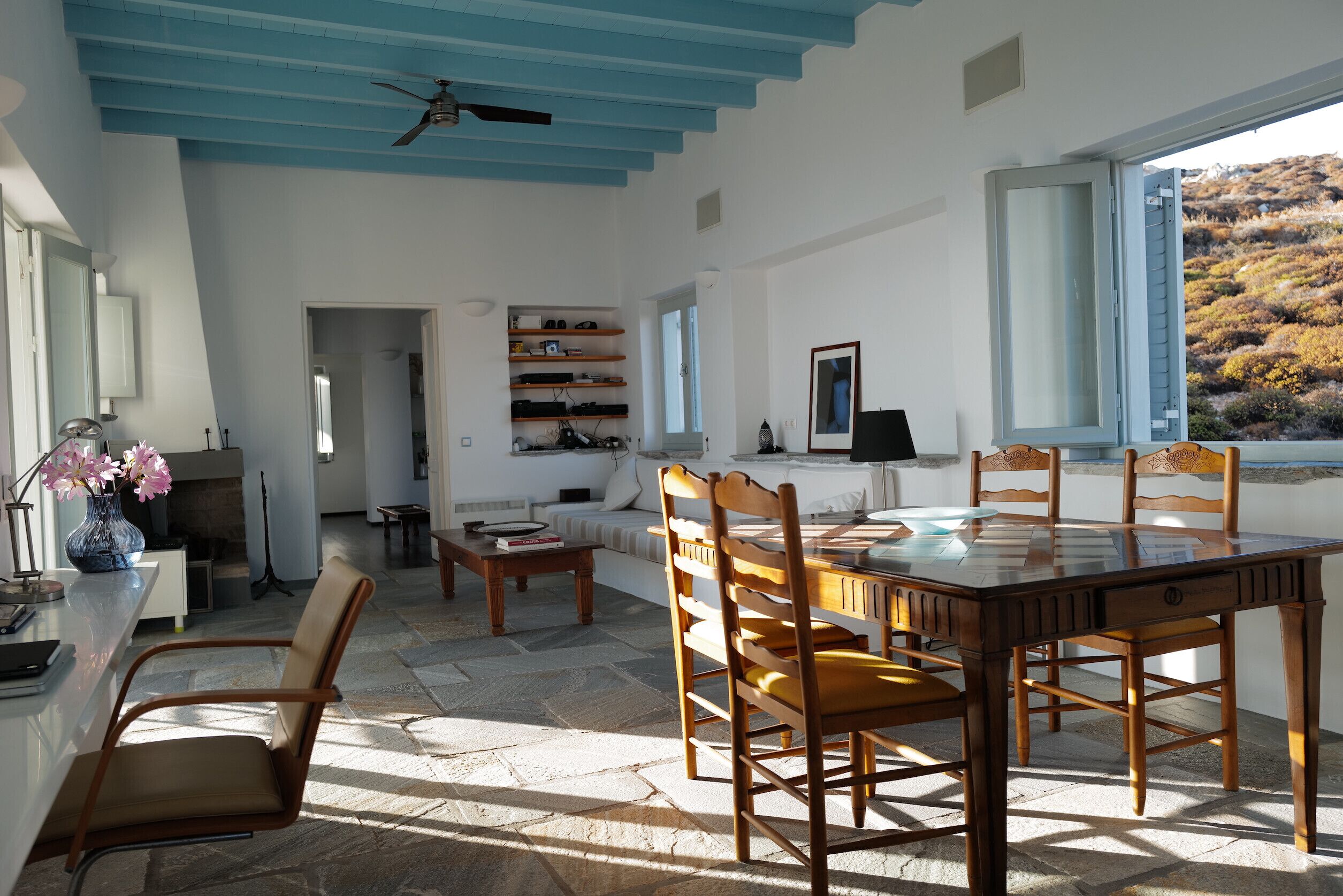 Un vaste espace dédié à la salle à manger, avec une table et des chaises en bois, un ventilateur de plafond et une vue sur l’extérieur par une fenêtre.