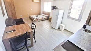 A compact living space with a kitchenette, a dining area, a bed with a colorful bedspread, and a small window. - Hidden Gem City Studio (Larnaca)