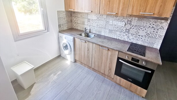 A compact kitchen with wooden cabinets, a washing machine, a sink, and an oven. - Hidden Gem City Studio (Larnaca)