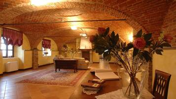 A spacious room with a high arched brick ceiling, a fireplace, a sofa, a coffee table, and a vase with flowers.