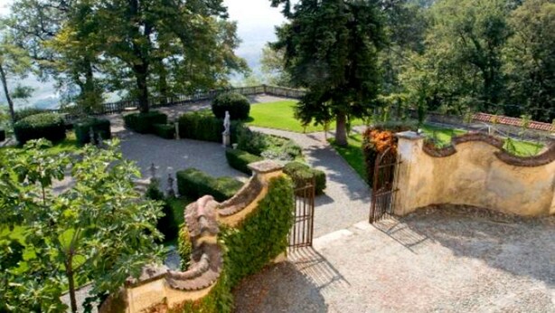 A landscaped garden with a curved wall, a statue, and a gate.