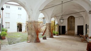 A courtyard with stone flooring, arches, and potted plants.
