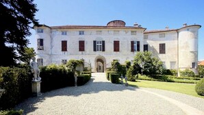 A large, historic building with a symmetrical facade, a central entrance, and a gravel driveway leading to the entrance.