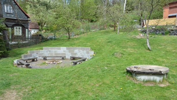 A grassy backyard with a stone fire pit and a concrete structure. - Family Chalet with Garden (Krásná Lípa)