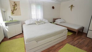 A bedroom with a large bed, a bedside table, a bench, a wardrobe, and a window with curtains. - Family Chalet with Garden (Krásná Lípa)