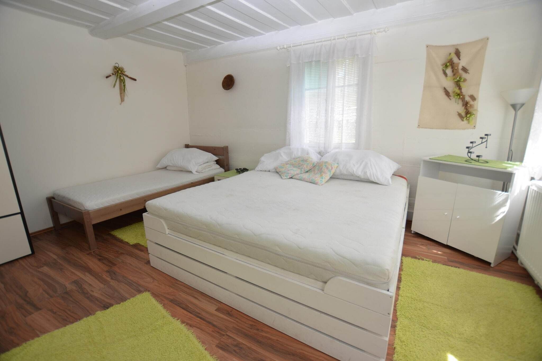 Une chambre à coucher avec un grand lit, un plus petit lit, une table de chevet, une lampe et un radiateur.