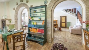 A room with a wooden table, chairs, a green cabinet with shelves, and a staircase in the background.