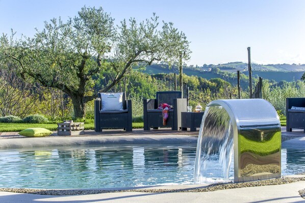 A pool area with a water feature, outdoor seating, and a view of the surrounding landscape.